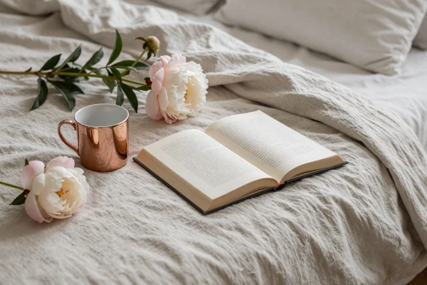 Linen bed flatlay with peony and book representing the best positions and intimacy techniques guide